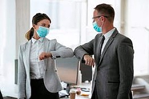 two workers practicing social distancing and wearing PPE after office reopening