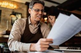 a business owner is elated analyzing his DBO insurance paperwork while working in a pub.