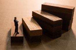 a figurine standing on the first step of wooden stair signifying business succession plan. Disability buy-out insurance protects business owners from certain disabilities.