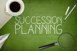 succession planning text written on green board. A cup of coffee, a magnifying glass, a paper plane and one each of a chalk and a pen is kept on each opposite corners.