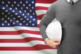 Man holding hard hat in front of flag