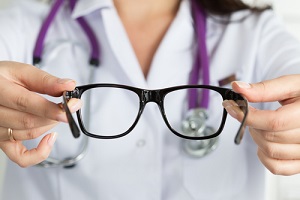 oculist doctor hands giving pair of black glasses to patient