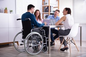 A group of four employees is discussing, one of them is sitting on a wheelchair