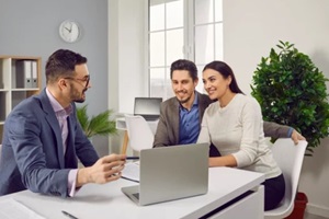 portrait of happy caucasian couple sitting with a business broker or insurance agent showing project on a laptop screen